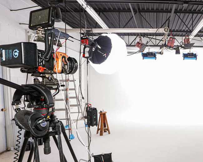 A photography studio setup with multiple cameras, lighting equipment, and a blank white backdrop.