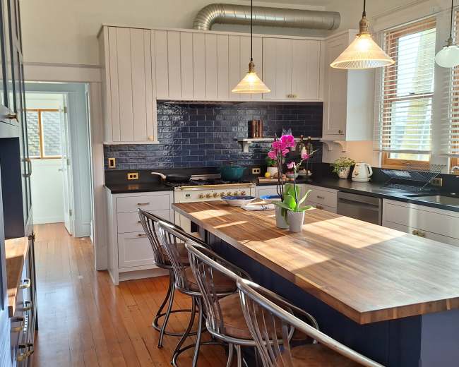 The image shows a modern kitchen featuring a central island with a wooden countertop, stainless steel appliances, and blue tile backsplash.
