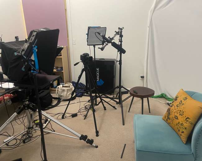The image shows a video recording setup with a chair, camera equipment, and lighting in a studio environment.