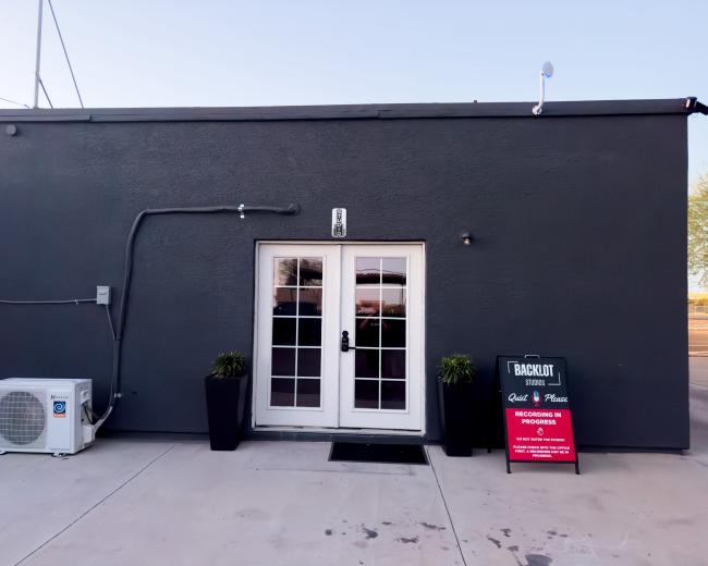 A gray building with a double-door entrance and a sign on a nearby stand.