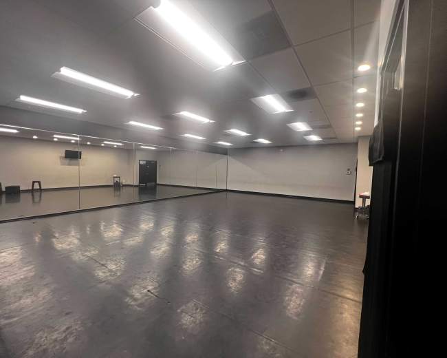 The image shows a spacious, well-lit studio with a large mirrored wall and polished black floors.
