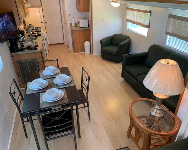 A small interior space featuring a dining table set for four, a sitting area with a couch and lamp, and a kitchenette in the background.