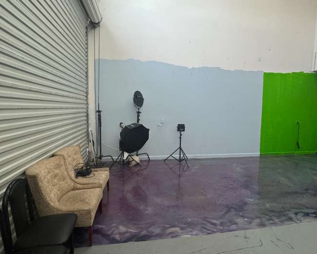 The image shows a sparse studio space with a couch, two light stands, and a green wall section.