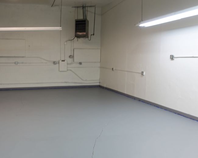The image shows a spacious, empty room with a gray floor and minimal overhead lighting.