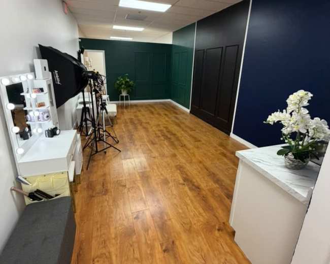 The image shows a well-lit hallway with wooden flooring, green and black accent walls, and photography equipment set up on the left side.
