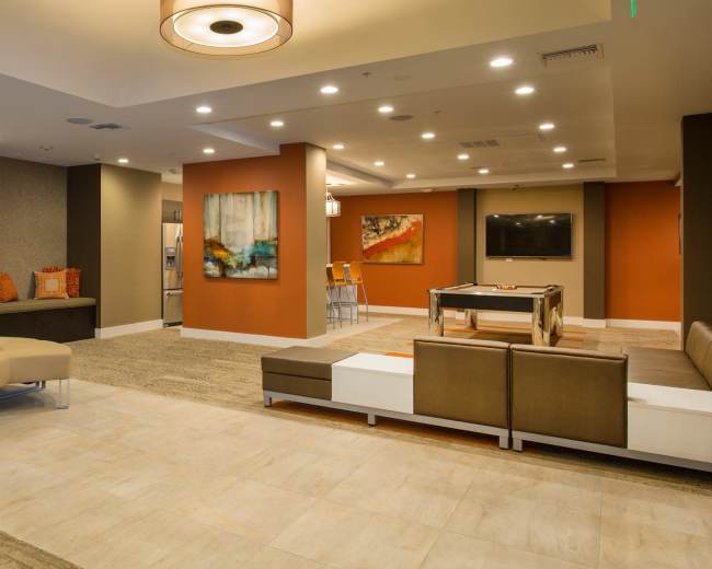 The image shows a modern lounge area with sofas, a round seating arrangement, an electric fireplace, and artwork on the walls.