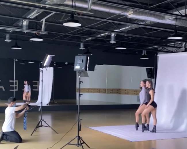 A photographer takes pictures of two models posing together in a studio with multiple lighting setups.