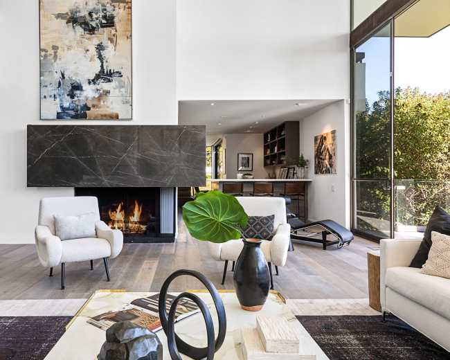 A modern living room with a minimalist design, showcasing a fireplace, large windows, and stylish furniture.
