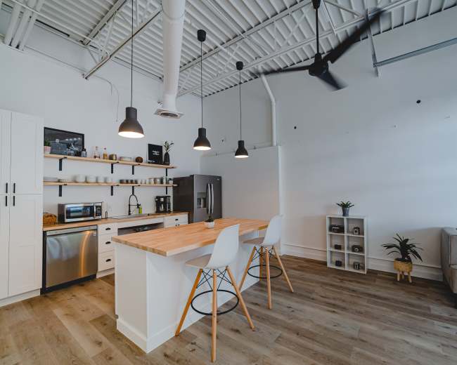 A modern kitchen features a large island with seating, stainless steel appliances, and open shelving against a white backdrop.