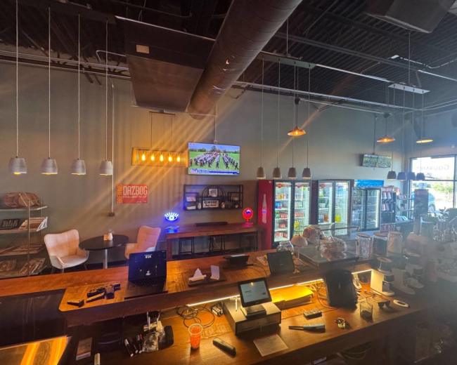 The image shows a bar area with a large screen displaying a sports event, overhead lights, and various seating options, along with a counter featuring a cash register and other equipment.