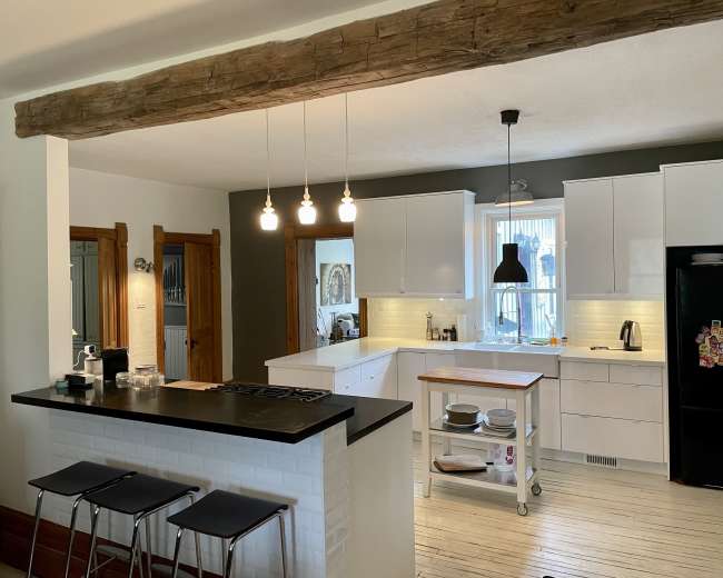 A modern kitchen features white cabinetry, a wooden beam overhead, and a central island with bar stools.
