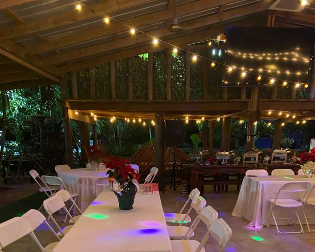 A decorated outdoor space features several tables and chairs, illuminated by string lights and colorful projections on the floor.