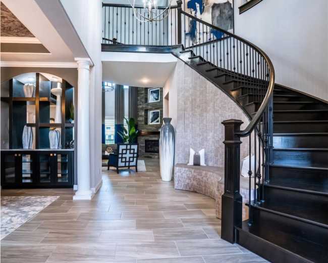 The image shows a spacious foyer featuring a curved staircase, large decorative vases, and a modern, open layout with natural light.