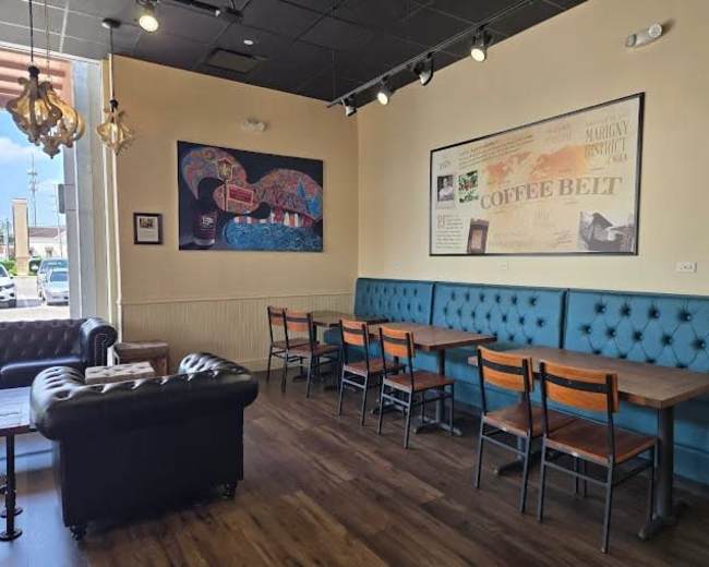 The image shows a coffee shop interior featuring tufted seating along the walls, wooden tables with chairs, and a decorative wall art display.