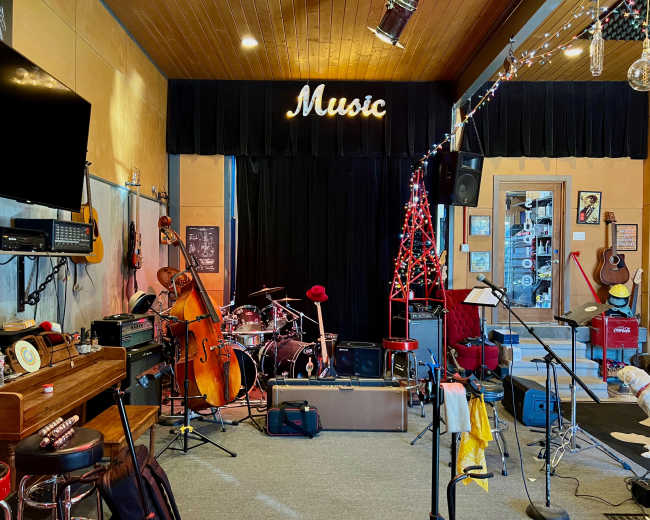 A music performance space is set up with various instruments, including a double bass and drum kit, along with a small stage and seating areas.