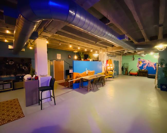 A spacious, well-lit room with concrete walls, several tables, and decorative murals on the walls.