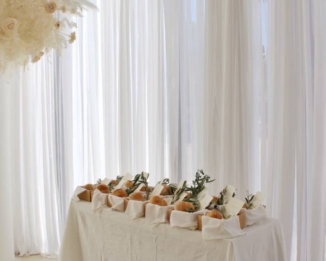 A banquet table adorned with neatly arranged plates of food is set against a backdrop of white drapery and soft lighting.