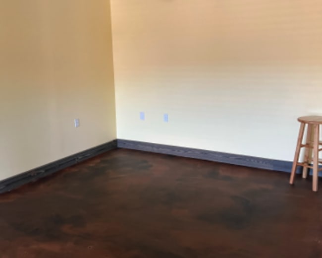 An empty room with yellow walls, a brown floor, and a wooden stool in one corner.