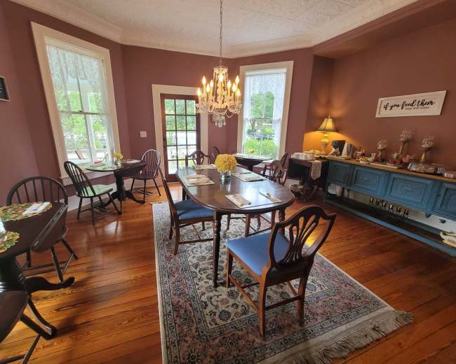A well-furnished dining room with several tables set for guests, a chandelier hanging from the ceiling, and a sideboard displaying food items.