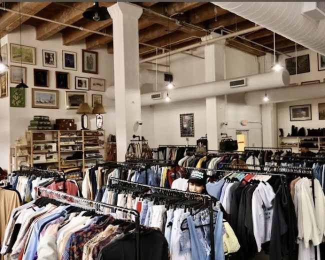 The image shows the interior of a thrift store with clothing racks filled with various garments and decorative items on the walls.