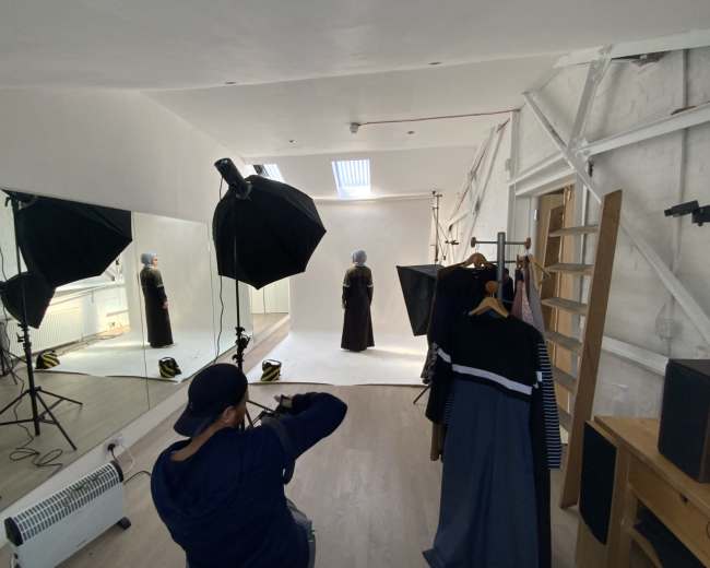 A photographer captures a model in a studio with a large mirror and clothing hanging on a rack in the background.