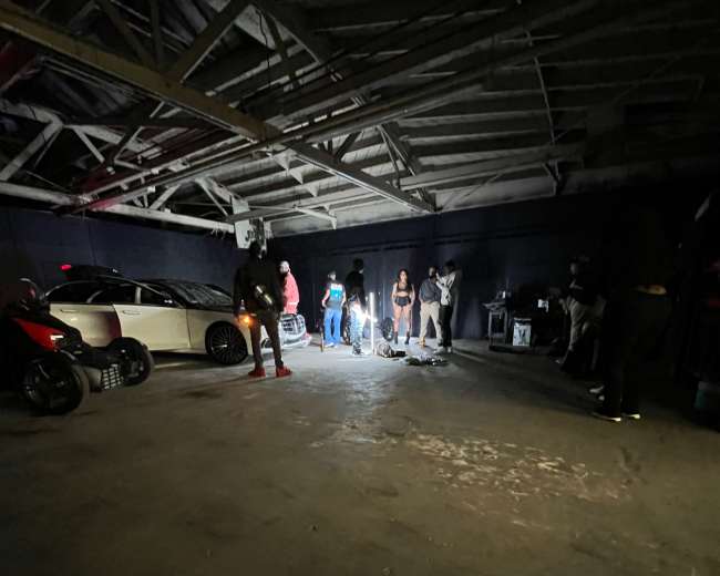 A group of people gathers in a dimly lit garage, illuminated by the glow of several lights.