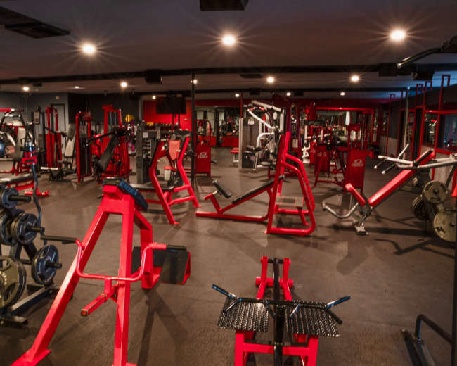 The image shows a well-equipped gym with various workout machines and weights arranged throughout the space.