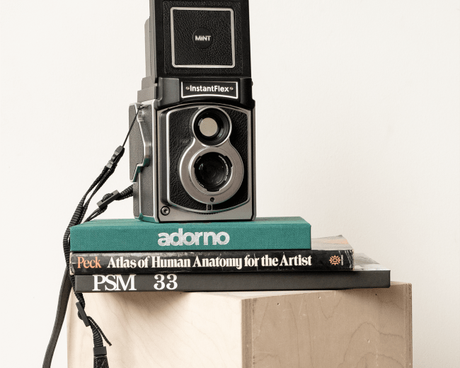 A vintage instant camera is placed on top of a stack of books on a wooden crate.
