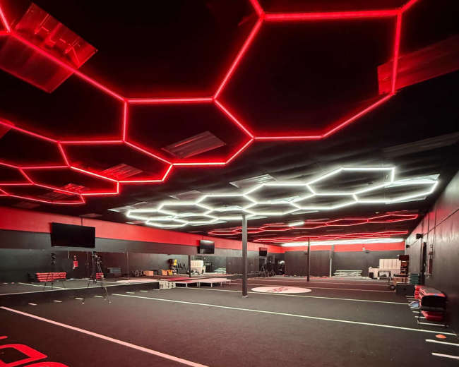 The image depicts a fitness or training facility with a dark floor, illuminated by red and white hexagon-shaped ceiling lights and various workout equipment scattered throughout the space.