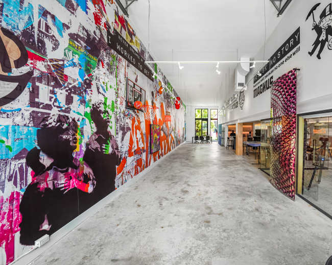 The image shows a spacious, modern interior hallway featuring vibrant wall art on one side and an open office area visible on the other.