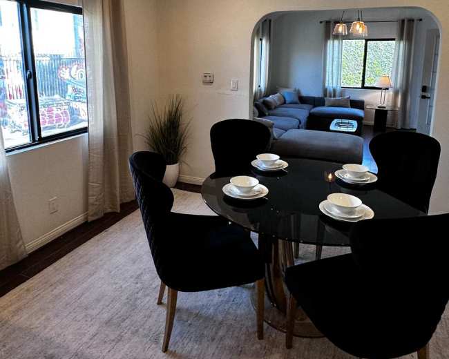 The image shows a dining area with a round black table set for four and a living room visible in the background.