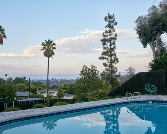 A swimming pool is nestled in a backyard with palm trees and a view of distant mountains under a clear sky.