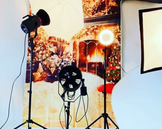 Studio lighting equipment arranged in front of a backdrop depicting a cozy indoor scene with a fireplace and Christmas decorations.