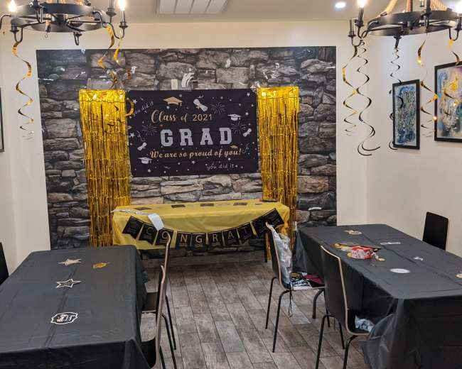A decorated room for a graduation celebration, featuring a black and yellow theme with tables, a festive banner, and wall decorations.
