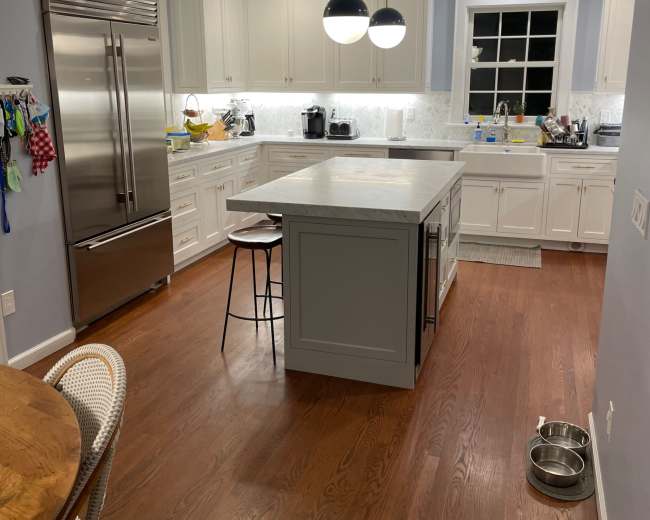 A modern kitchen features white cabinetry, stainless steel appliances, and a central island with a light gray countertop.
