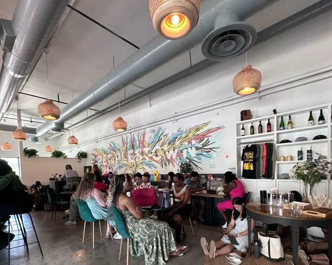 A vibrant café features a mural on the wall, with patrons seated at various tables and enjoying their time.