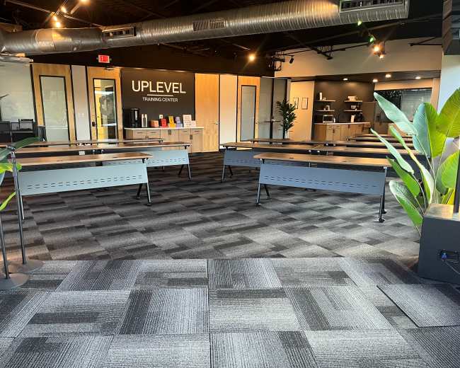 The image shows the interior of a training center with multiple tables arranged in a spacious layout and modern furnishings.