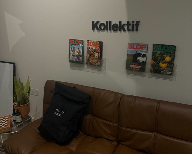 The image shows a modern sitting area with a brown leather couch, a plant in a pot, and three magazines titled "SLOP" displayed on the wall.