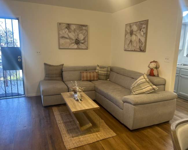 The image shows a modern living room with a gray sectional sofa, a wooden coffee table, and two floral wall artworks above the couch.
