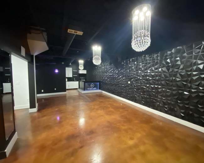 A modern, empty interior space with textured black walls, pendant chandeliers, and polished concrete flooring.