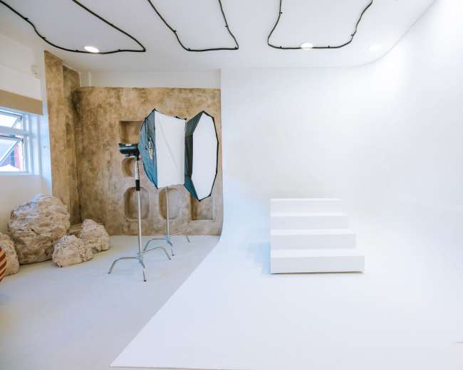 The image shows a photography studio featuring a white seamless backdrop, a set of white steps, and a light source with an umbrella modifier.