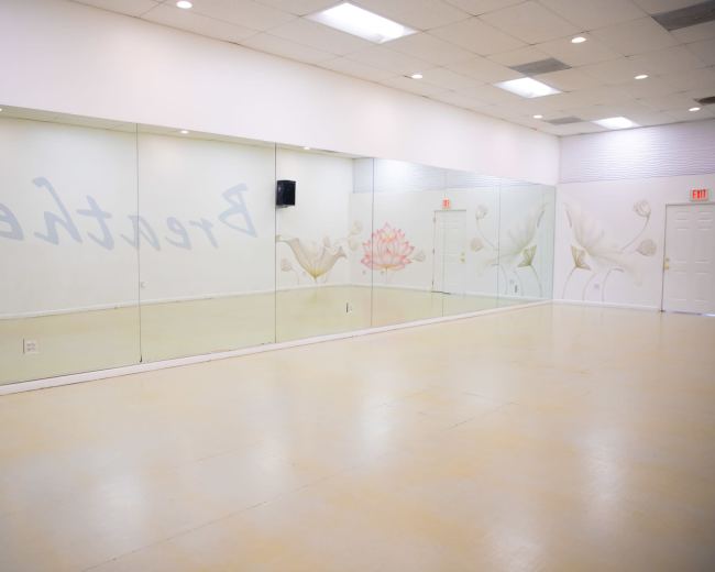 The image shows a spacious dance studio with mirrored walls and light-colored flooring, featuring a decorative mural of flowers.