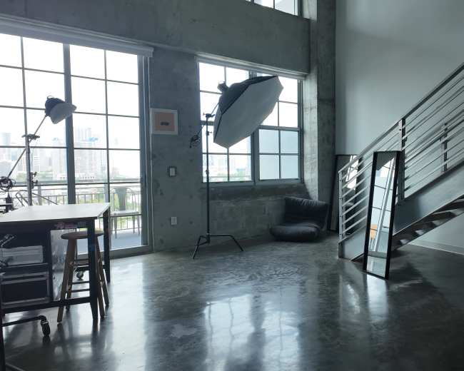 An industrial-style room with large windows, a staircase, a mirror, a desk, and a bean bag chair.