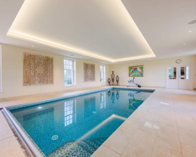 An indoor pool area with tiled flooring, elegant lighting, and decorative wall art surrounding the pool.