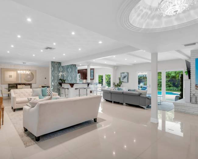 The image shows a modern open-concept living space with a cozy seating area, a dining area, and a view of a pool through large windows.