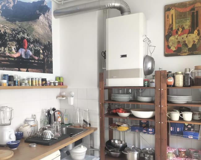 The image shows a cluttered kitchen with a wooden counter, an assortment of dishes, and a large poster on the wall depicting a person overlooking a mountainous landscape.