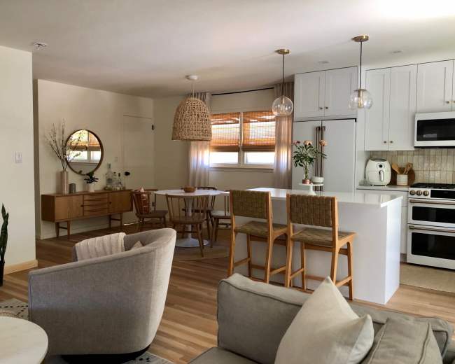 The image shows a modern, open-concept living space with a kitchen island, dining area, and comfortable seating arranged around a coffee table.