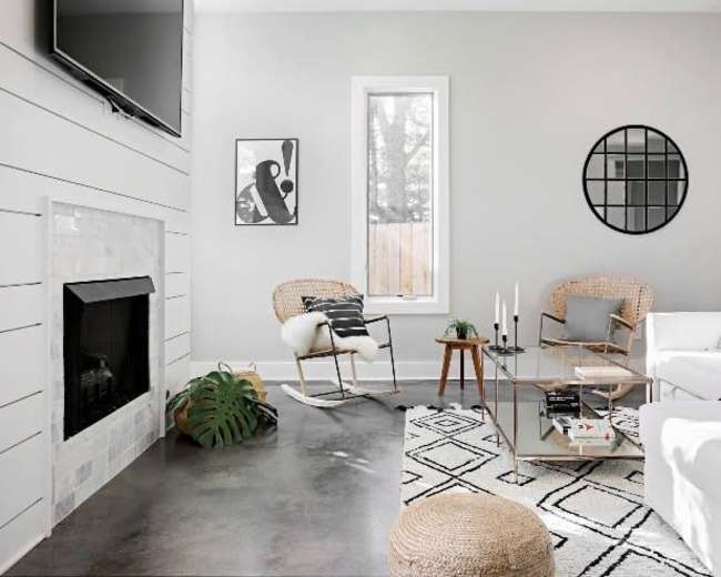 A modern living room featuring a white sofa, a glass coffee table, a fireplace, and a large window, all set against light gray walls.