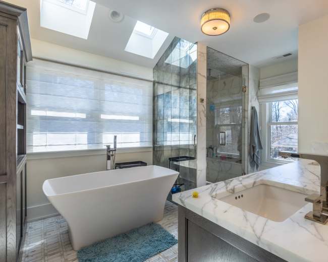 The image shows a modern bathroom featuring a freestanding bathtub, a glass shower enclosure, and a marble countertop with dual sinks.