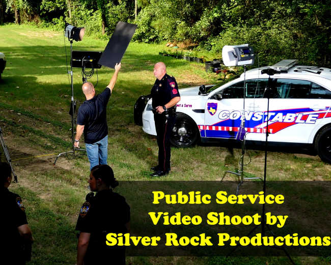 A group of people is filming a public service video in a grassy area, featuring law enforcement personnel and production equipment.